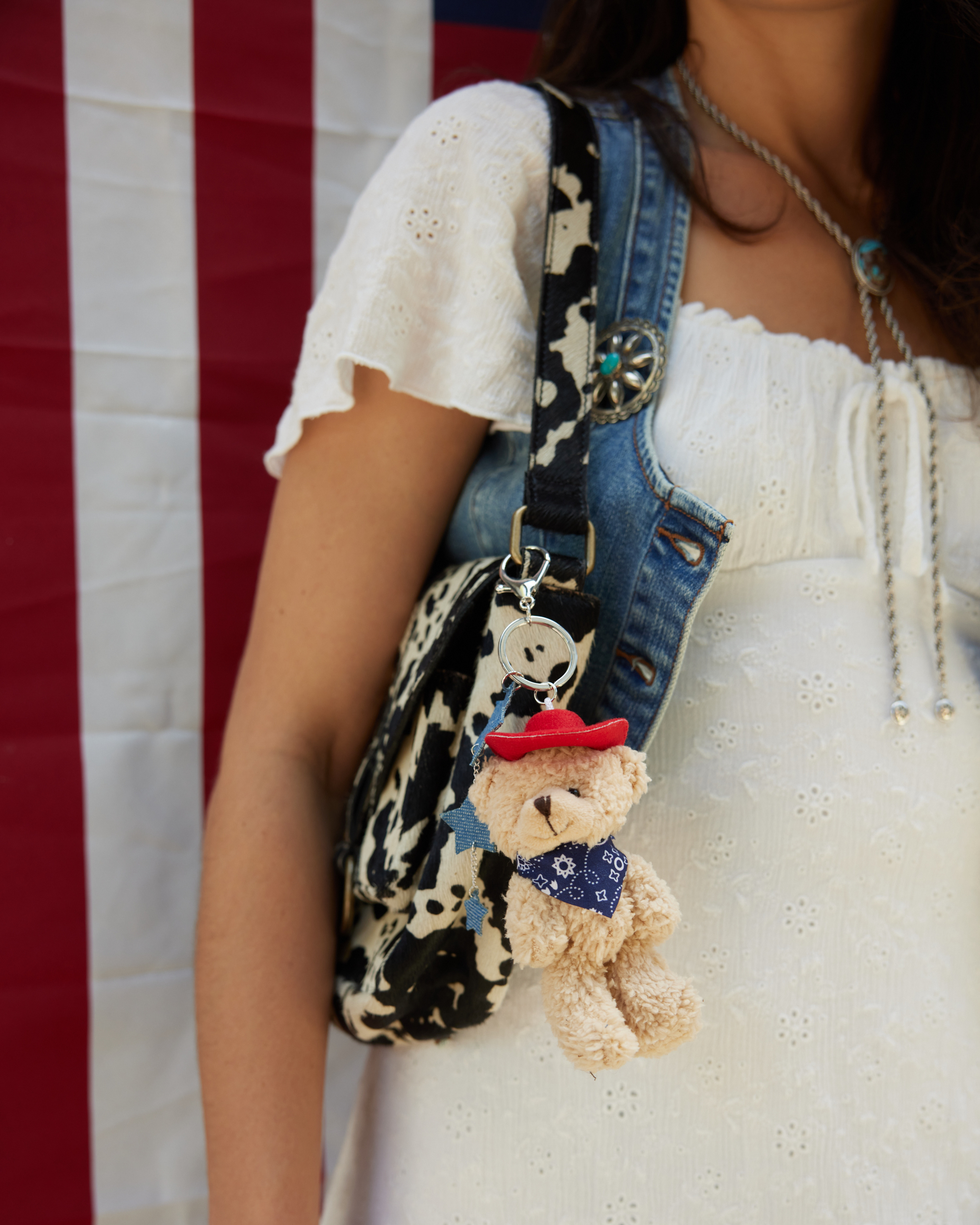 A cowprint purse with teddy bear charm